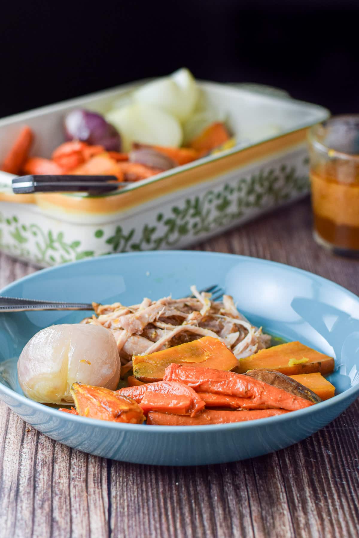 A blue dish with the vegetables on it along with pork. There is a baking dish of the vegetables in the back