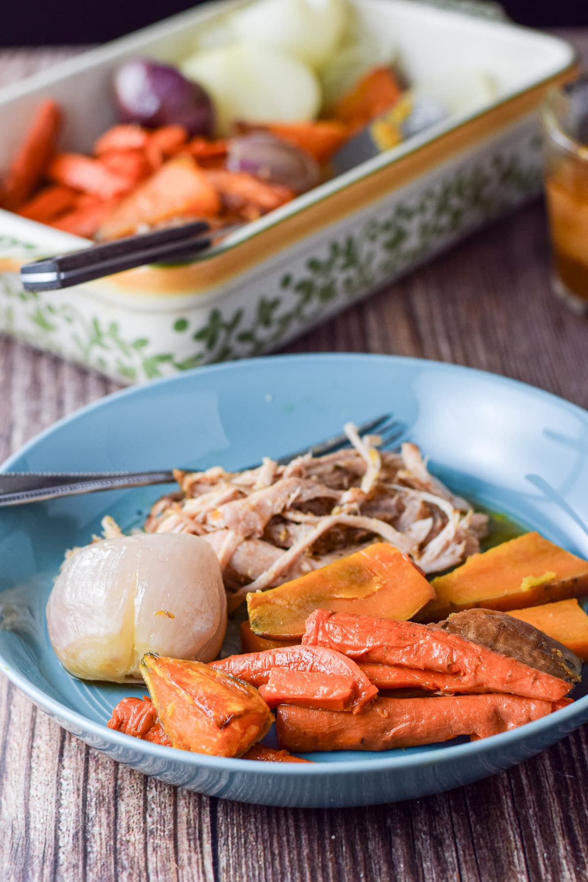 A deep blue dish with baked vegetables and pulled pork, along with a baking dish filled with more vegetables