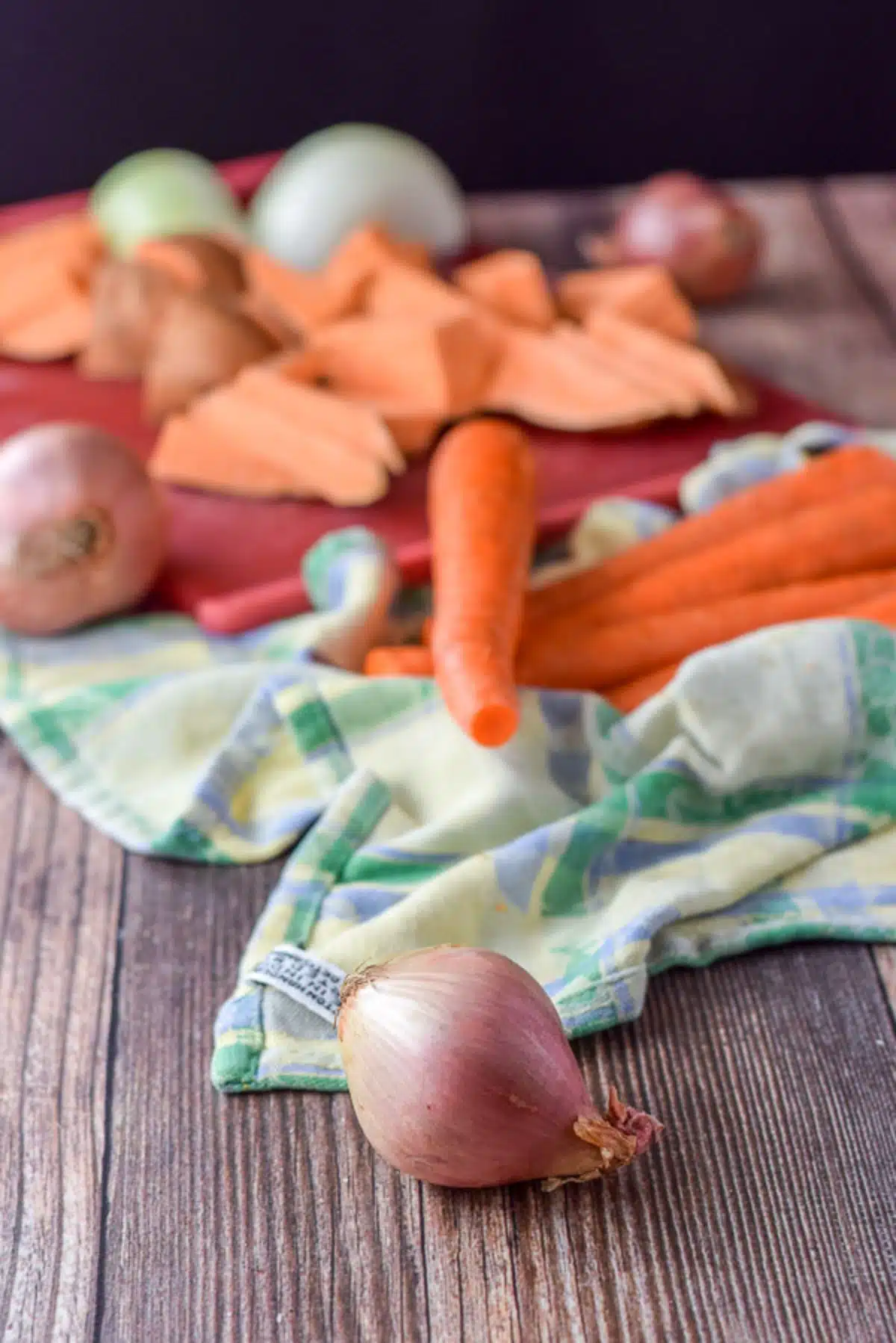 shallots, carrots, sweet potatoes and onions on a colorful towel and on a wooden table