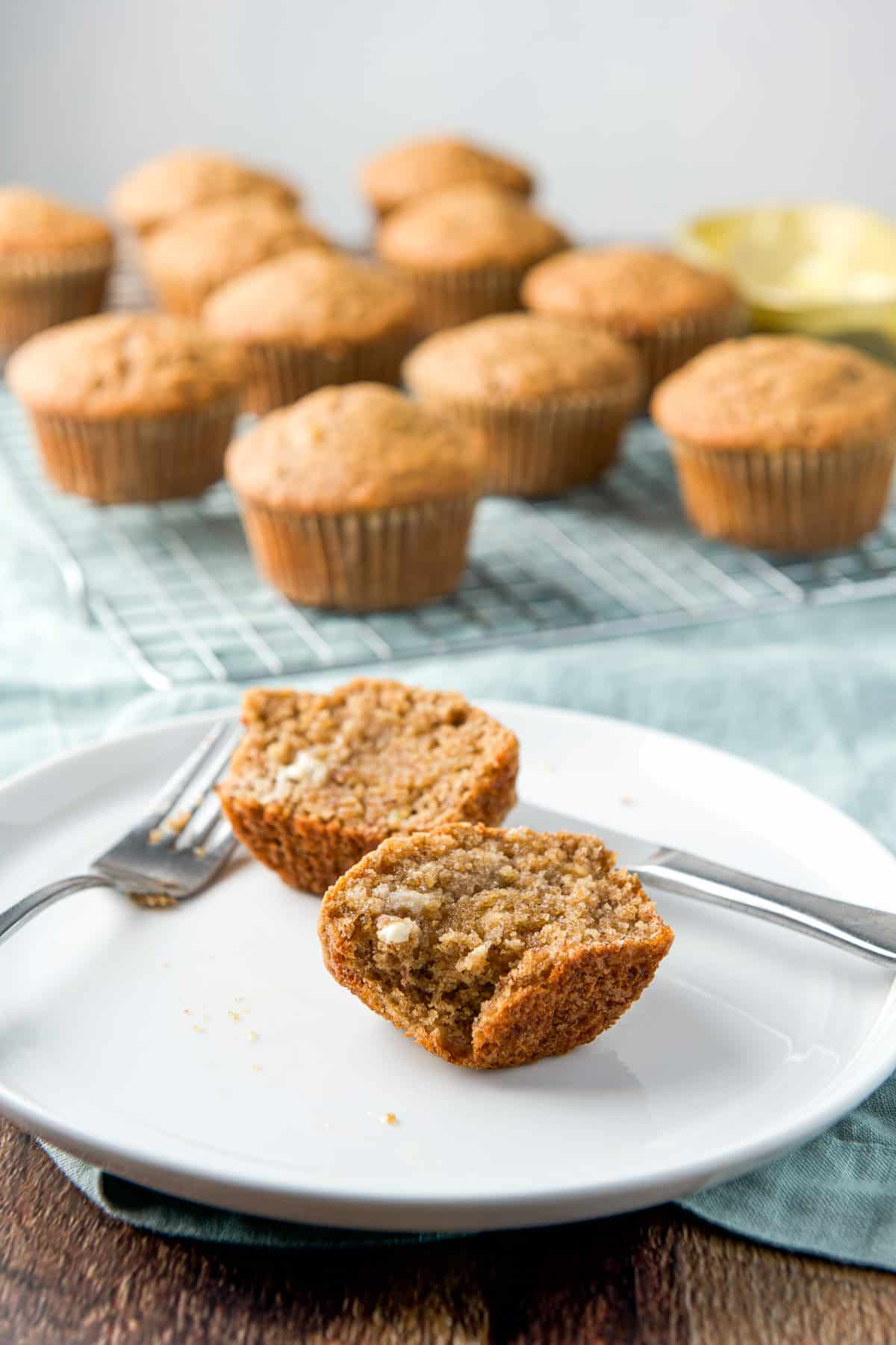 A plate with two halves of a muffin both with butter melted on it. In the back are more muffins on a rack