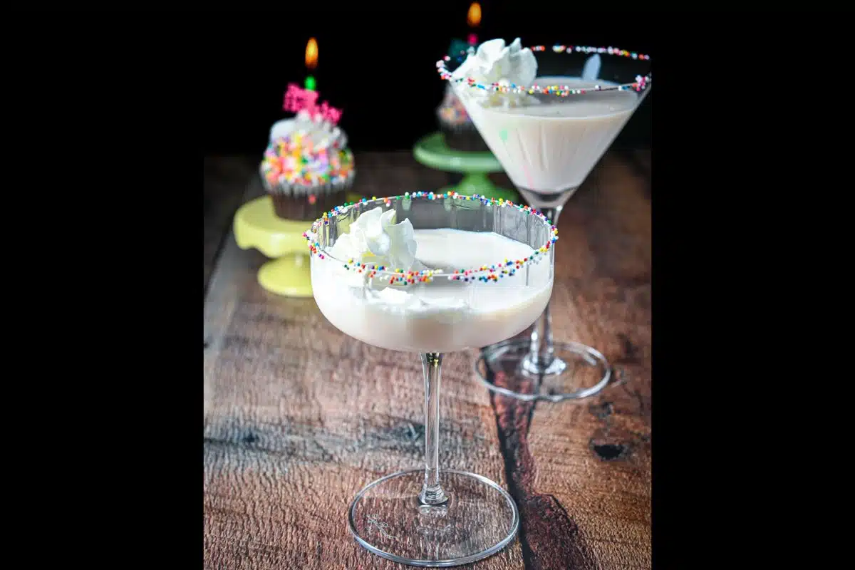 Two martini glasses filled with a cream drink with two cupcakes in the back