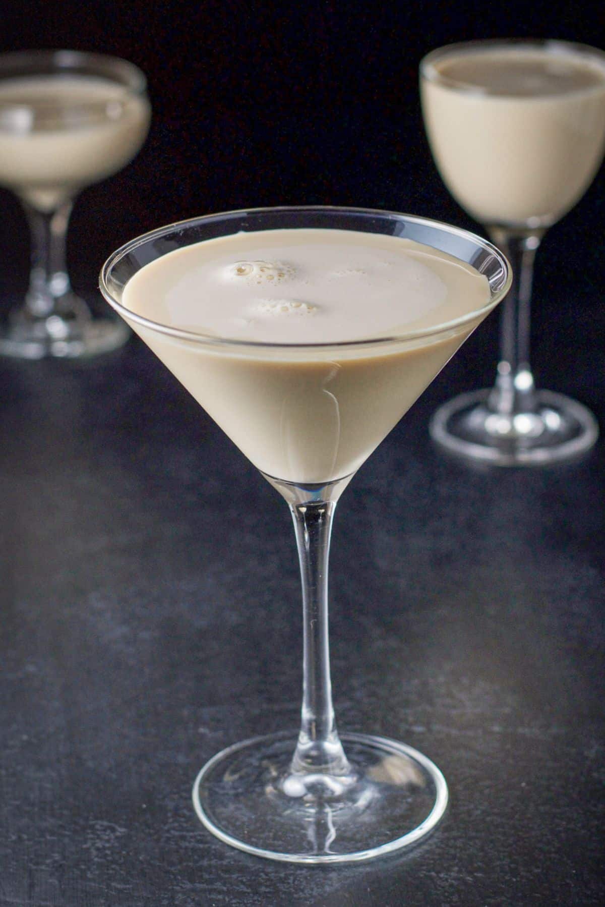 Classic martini glass filled with the creamy drink in front with the other two glasses in the background