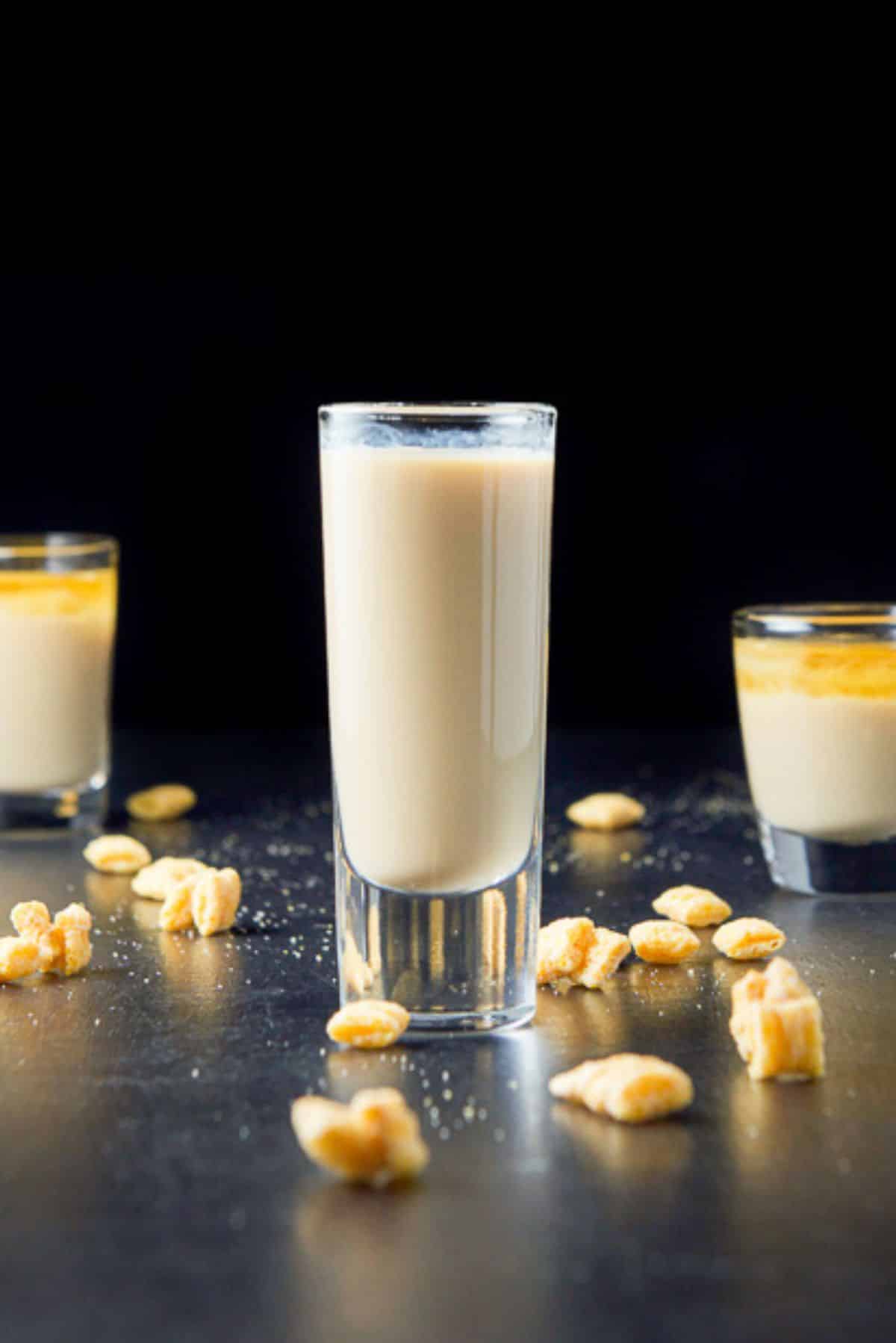 Tall glass in front filled with the shot. It looks mixed while the other two are layered. There is cereal on the table