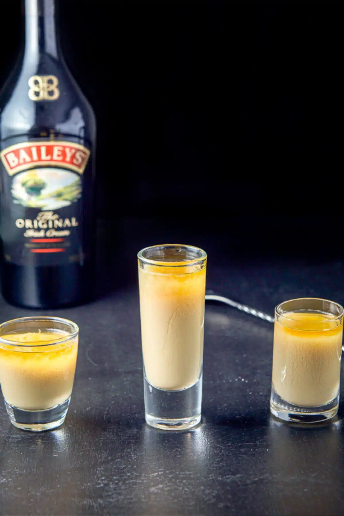 Irish cream layered into the glasses with the spoon and bottle in the background
