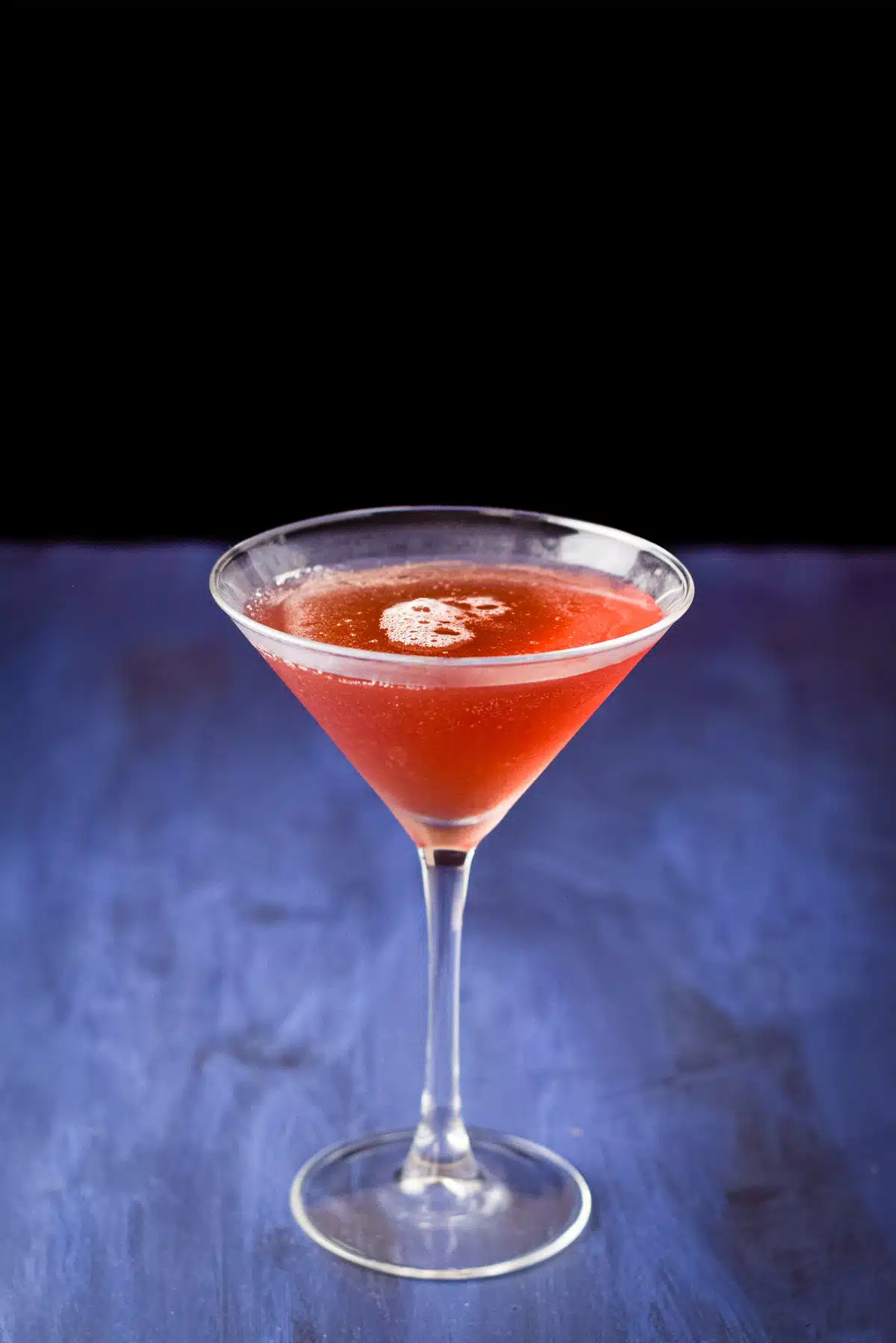 The red drink in a martini glass on a blue table and black background
