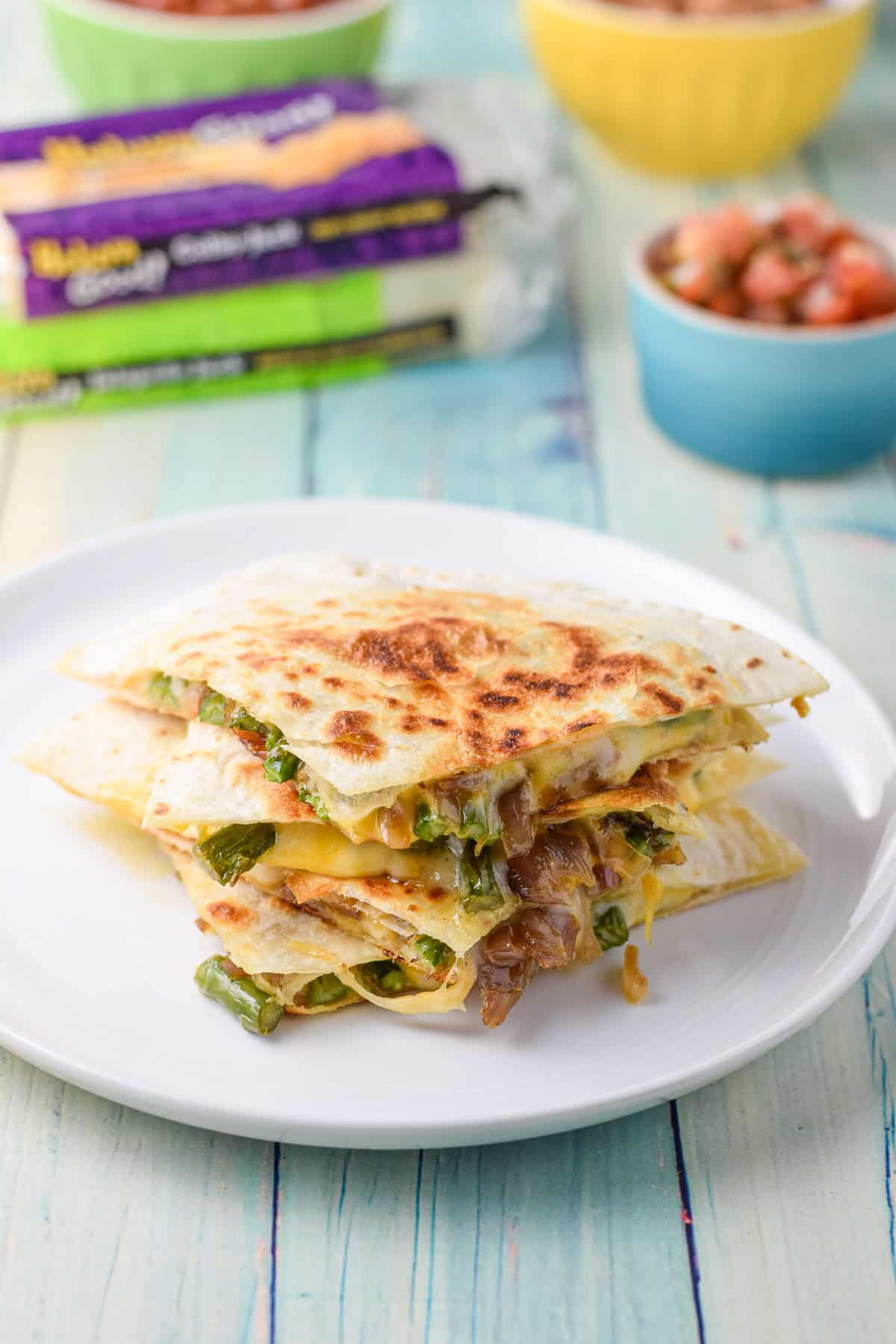 A white plate with the vegetable quesadillas on the table with cheese and salsa