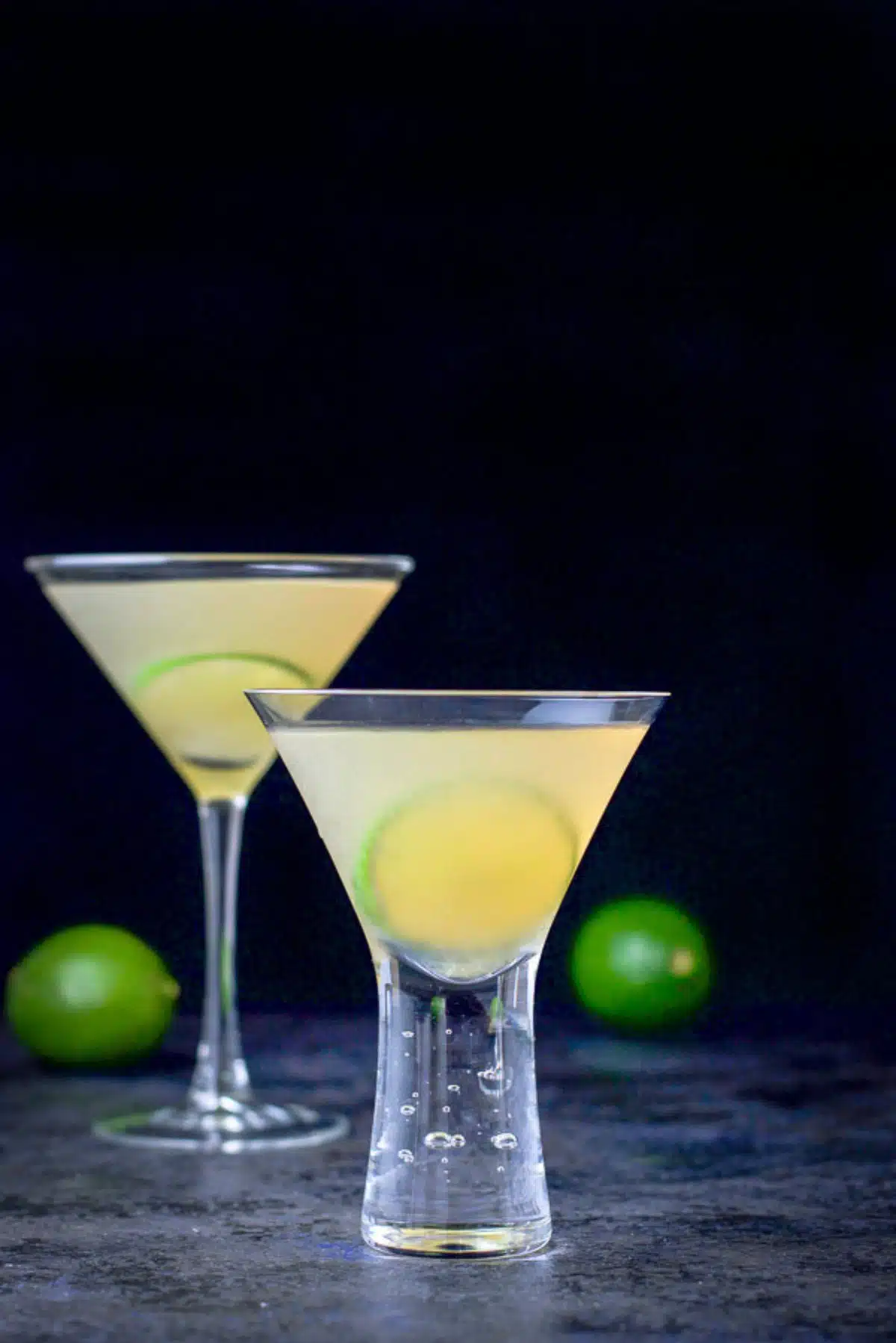 vertical view of the bubble martini glass in front of the classic glass with a few limes in back