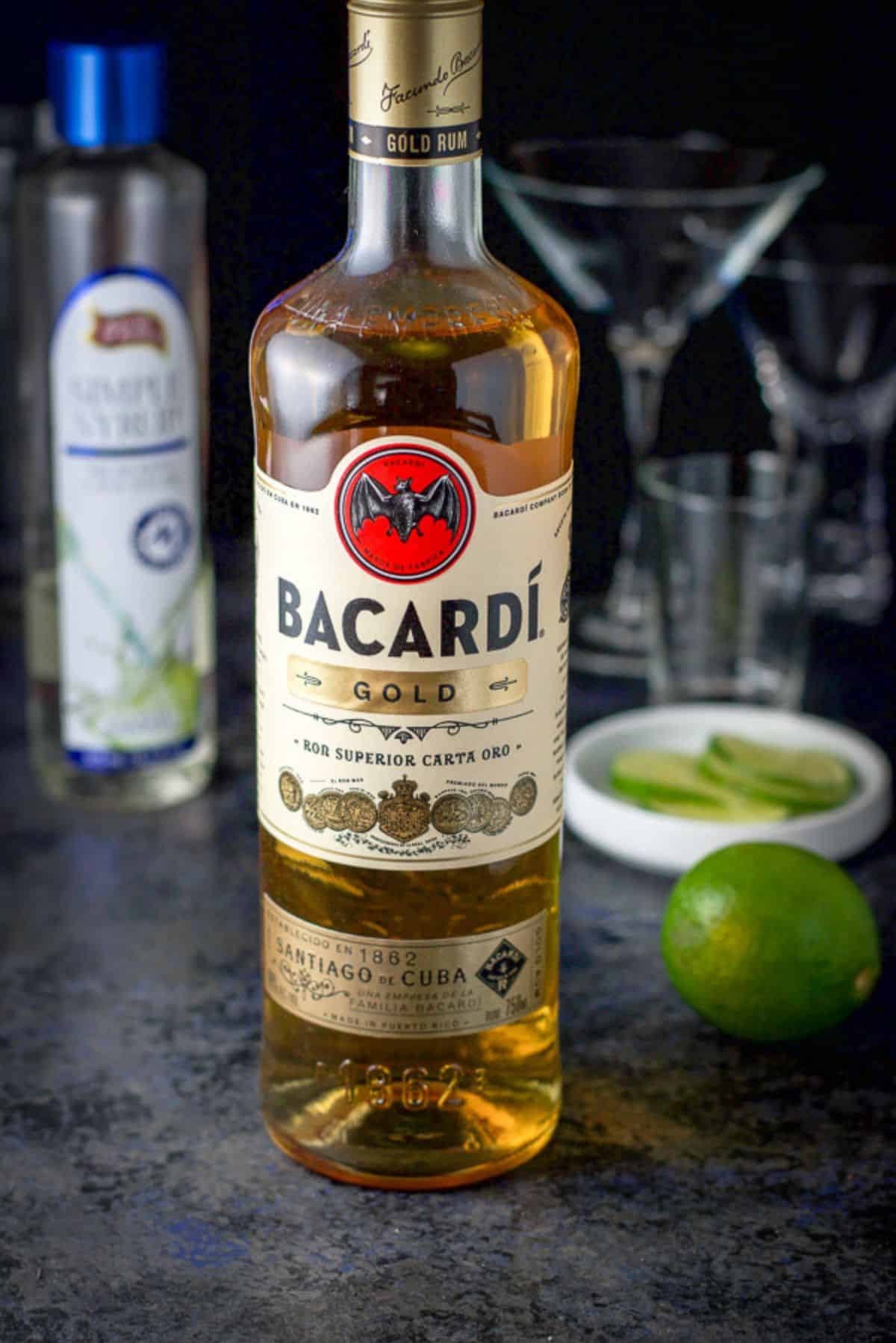 The ingredients: gold rum, simple syrup, and lime on a table with the glassware