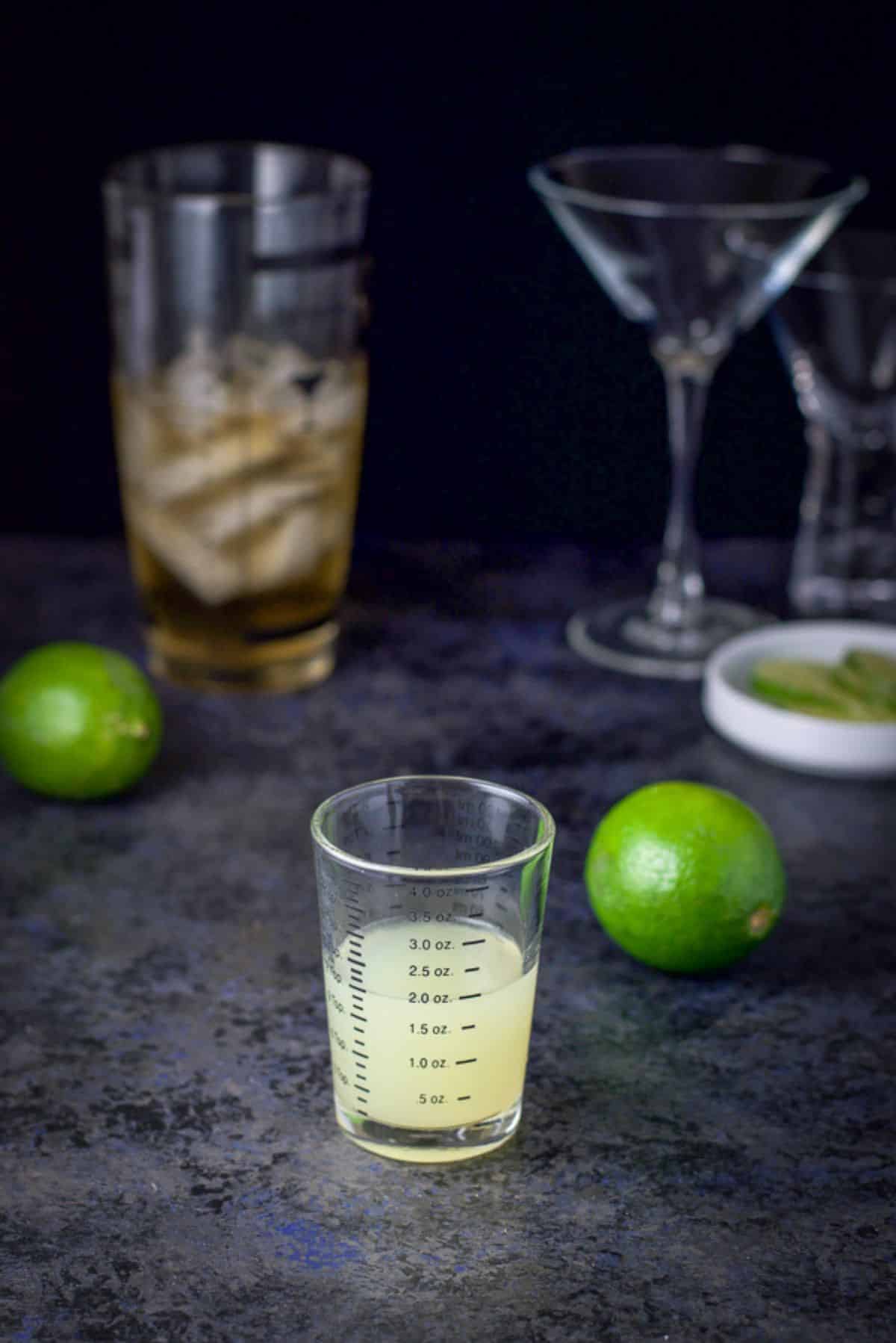 Lime measured out with other limes on the table along with the cocktail shaker in the background