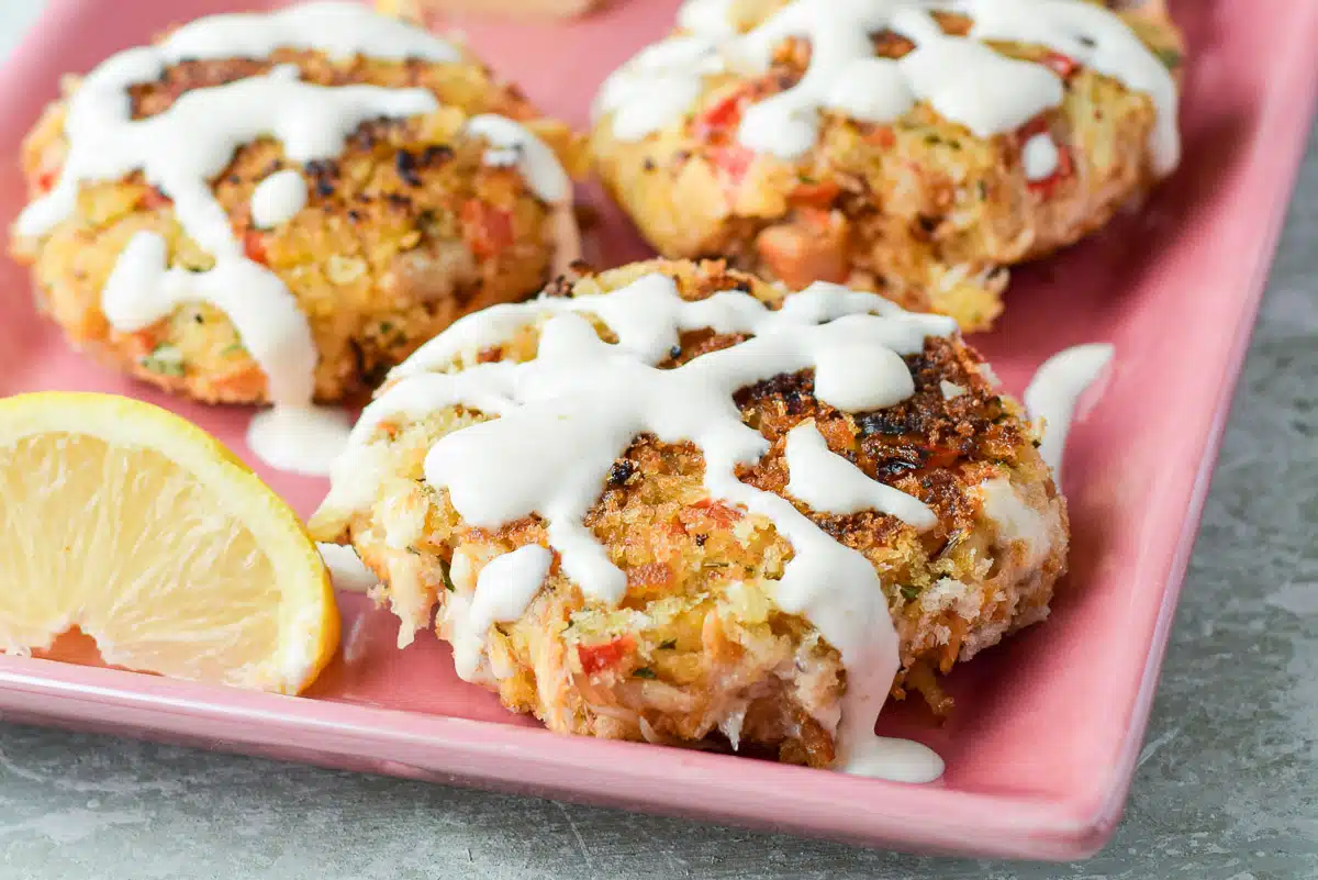 A pink platter with crab cakes on it with drizzle and lemon