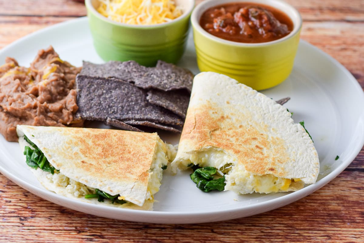 A white plate with the seafood quesadilla, beans, chips, cheese and salsa