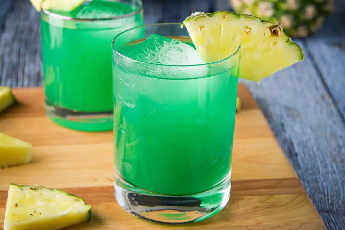 close up of two green cocktails on a board with pineapple as garnish