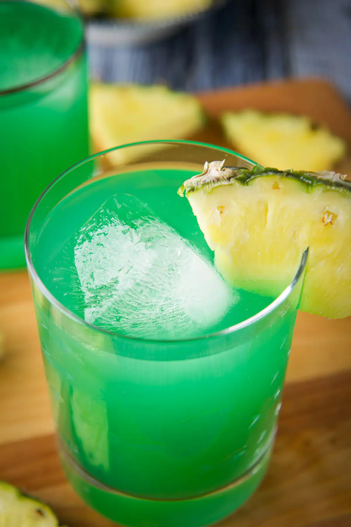 Close up of a glass of drunk leprechaun with a pineapple wedge on the rim. There is also another drink in the back with pineapple wedges