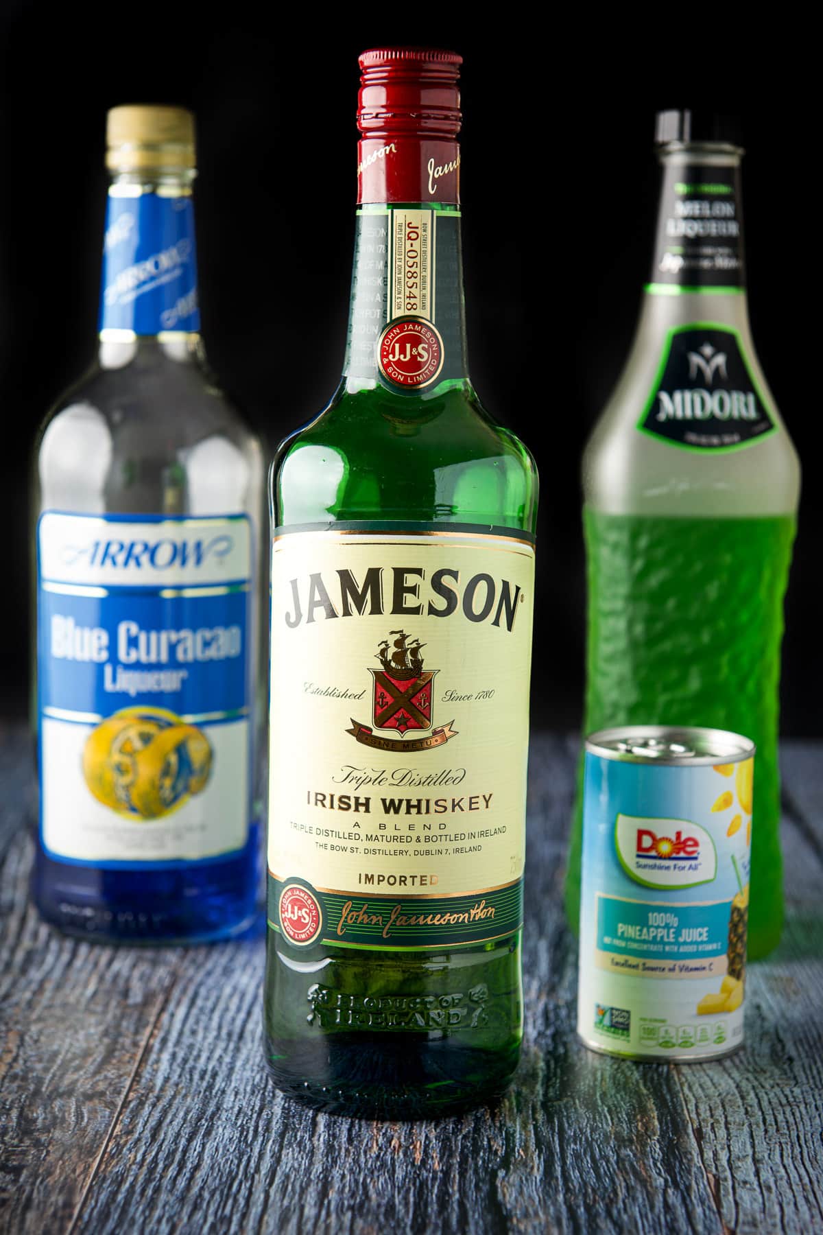 Whiskey, blue curacao, midori, and pineapple juice on a blue table