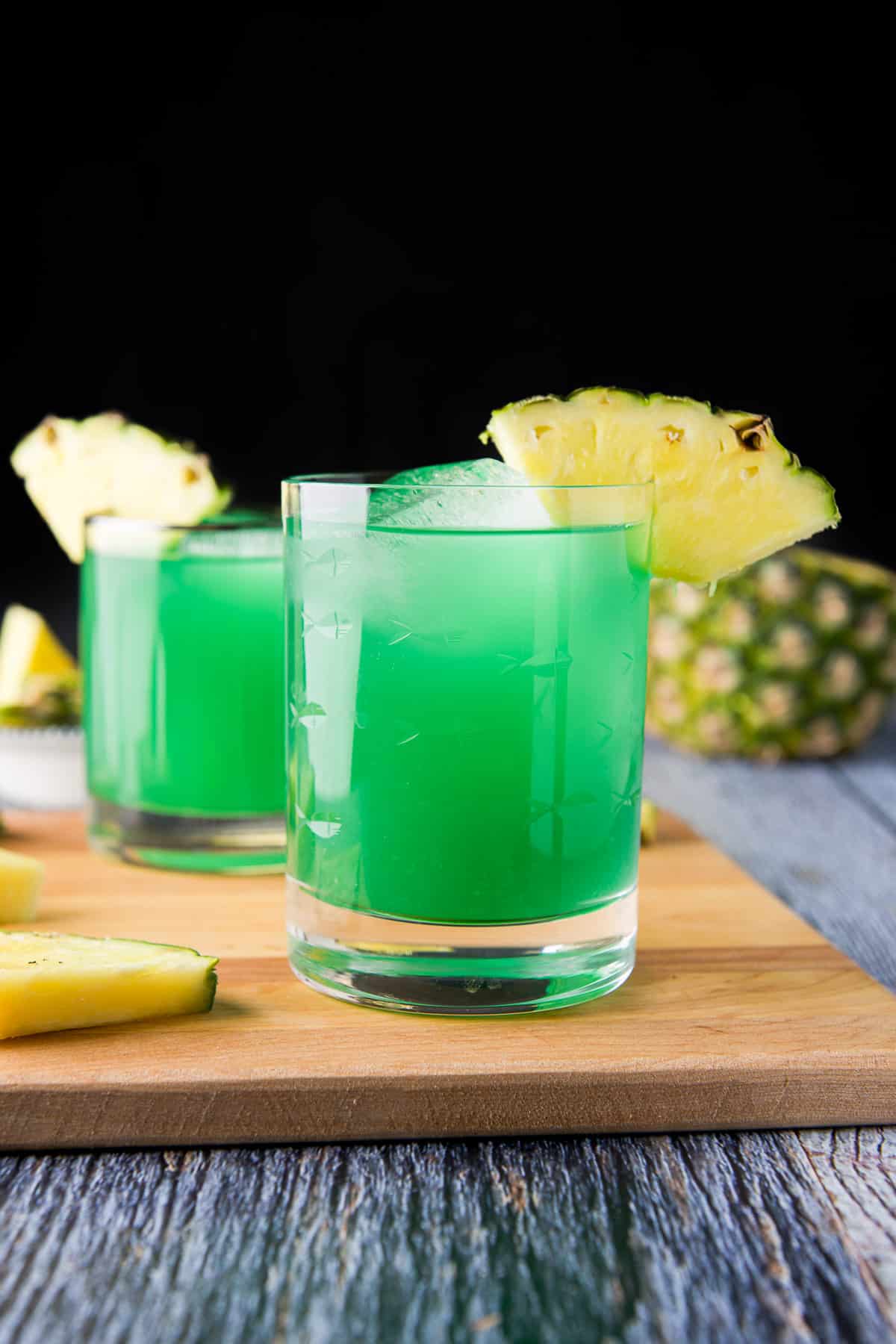 a board on the table with the two green drinks with pineapple wedges as garnish on the glasses