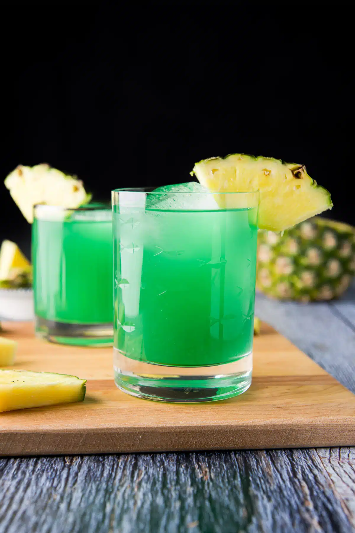 a board on the table with the two green drinks with pineapple wedges as garnish on the glasses
