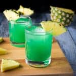 a square photo of the green drink in glasses with pineapple wedges as garnish
