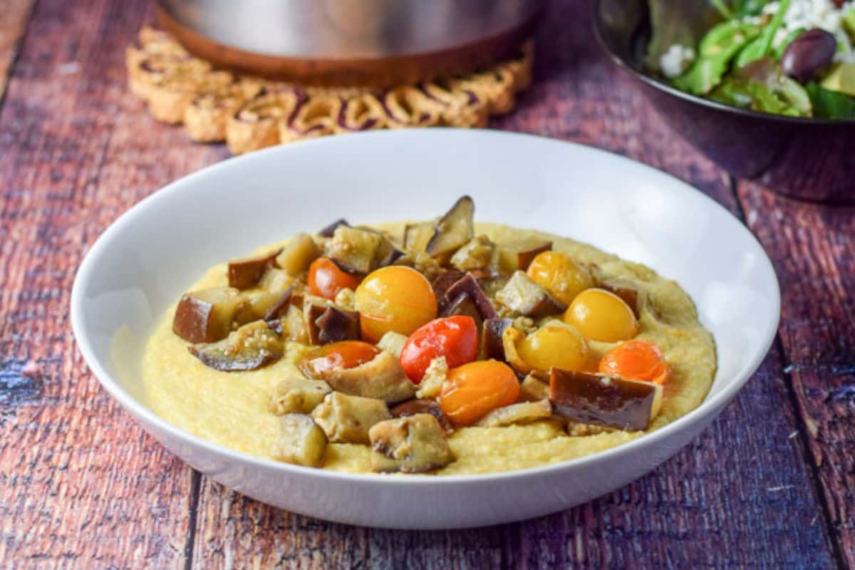 Cooked tomatoes and eggplant on the polenta with a salad and pan in the back