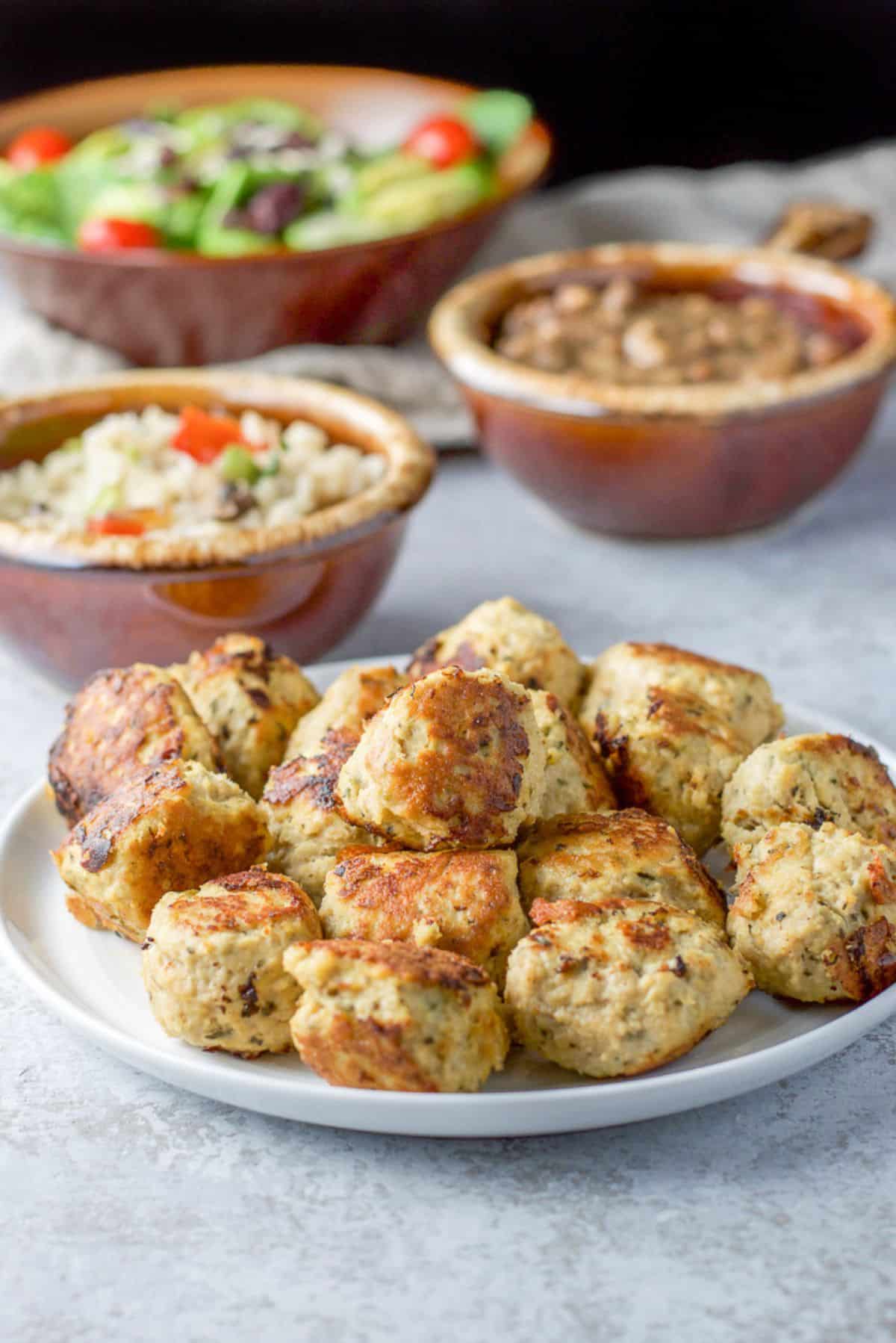 A white plate with a pile of meatballs and behind there is a salad, rice, and beans