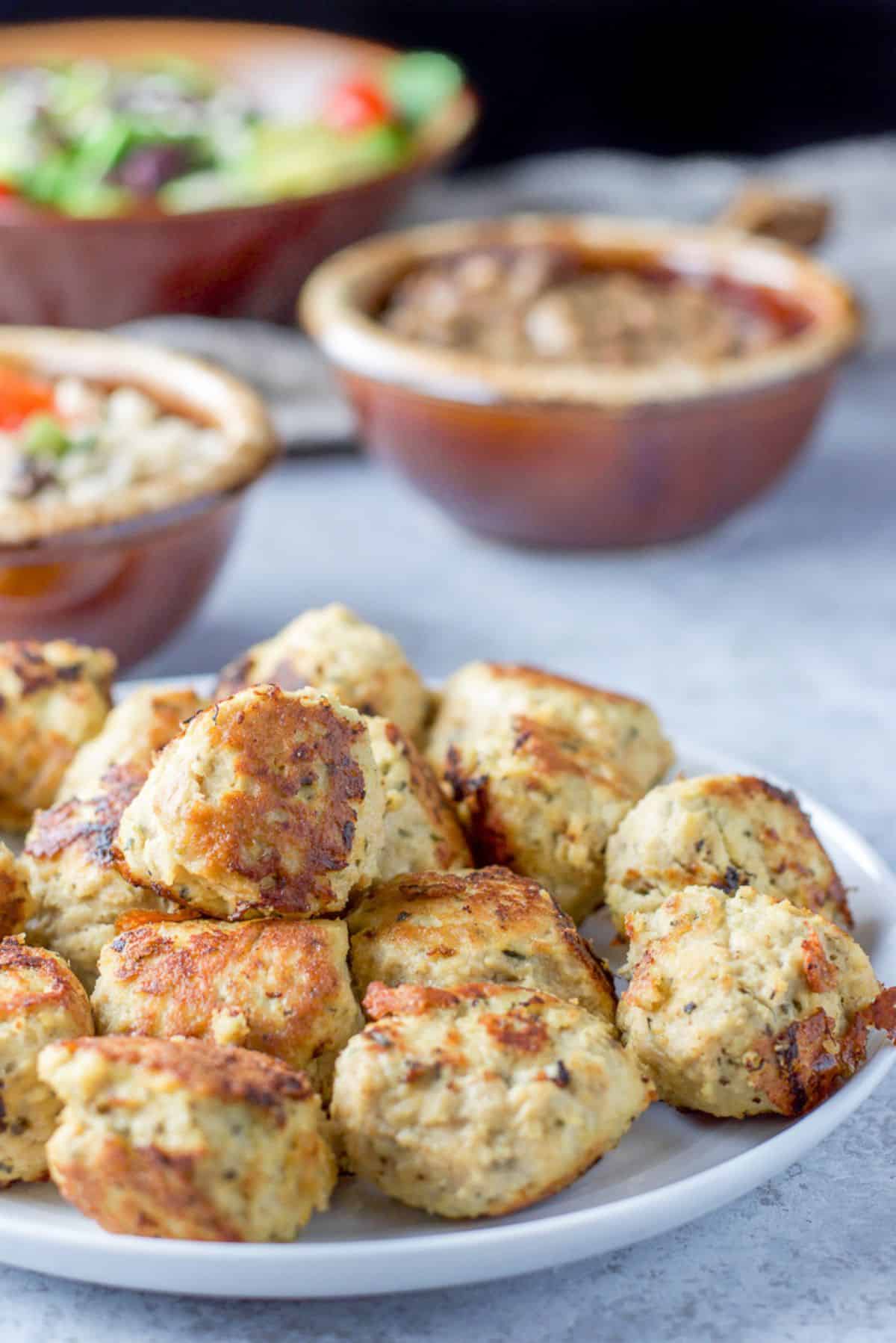 A close view of a pile of meatballs on a plate with a few crocks in back filled with sides