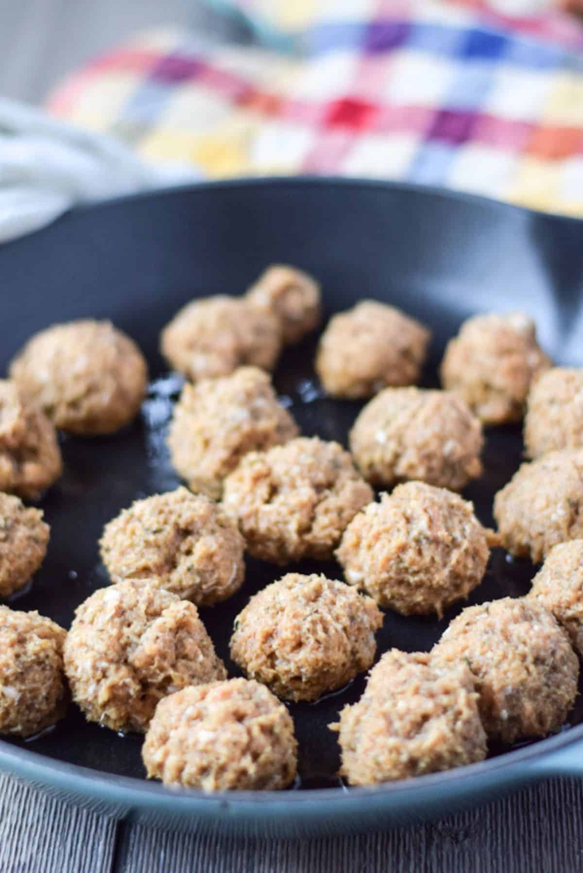 A cast iron skillet with raw chicken meatballs in it