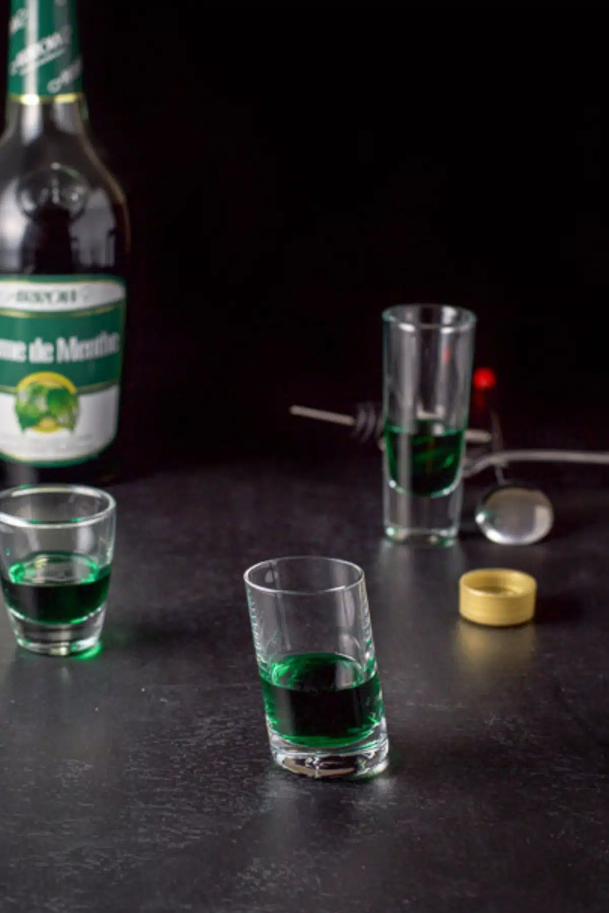 Green creme de menthe poured into the shot glasses with the bottle in the background