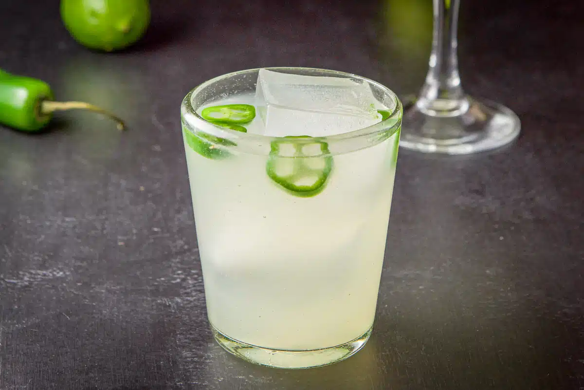 A double old fashioned glass filled with a margarita with jalapenos in it - horizontal