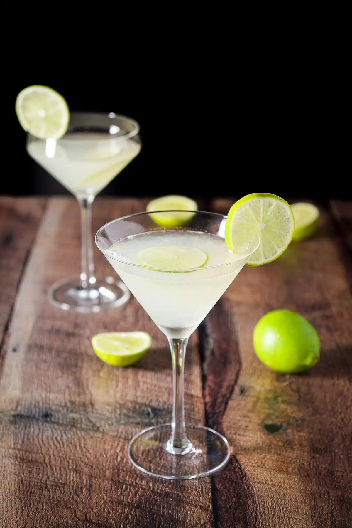 A beveled regular martini glass with another fun glass filled with the martini and garnished with lime wheels