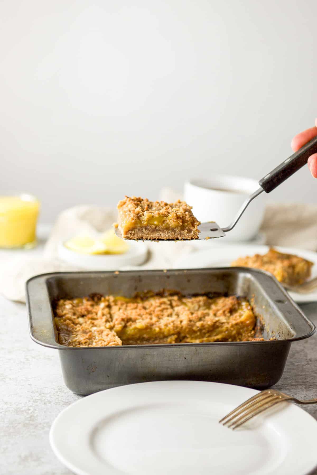 A piece of the lemon bar being lifted out of the pan and over a plate with a fork on it