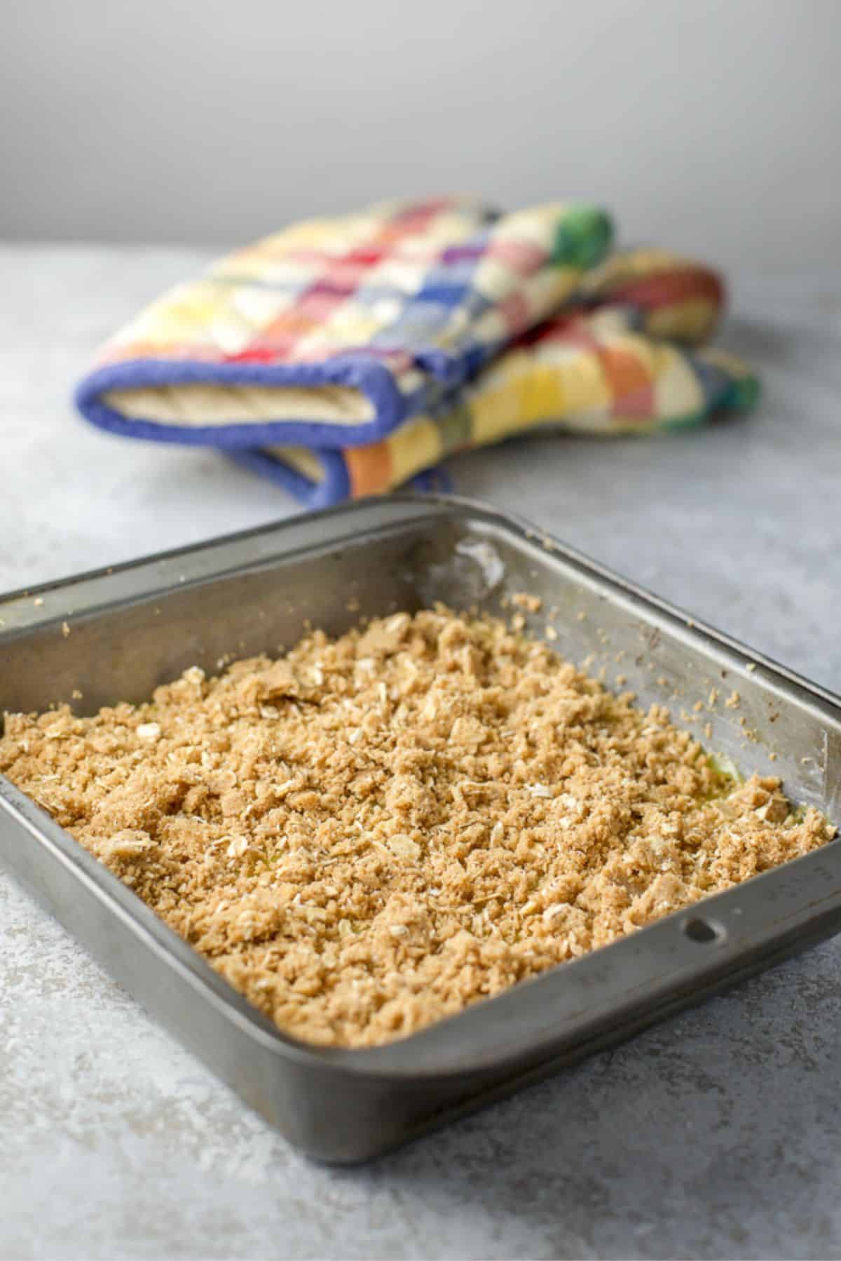 Freshly baked lemon bars in a square pan with two oven mitts in the background