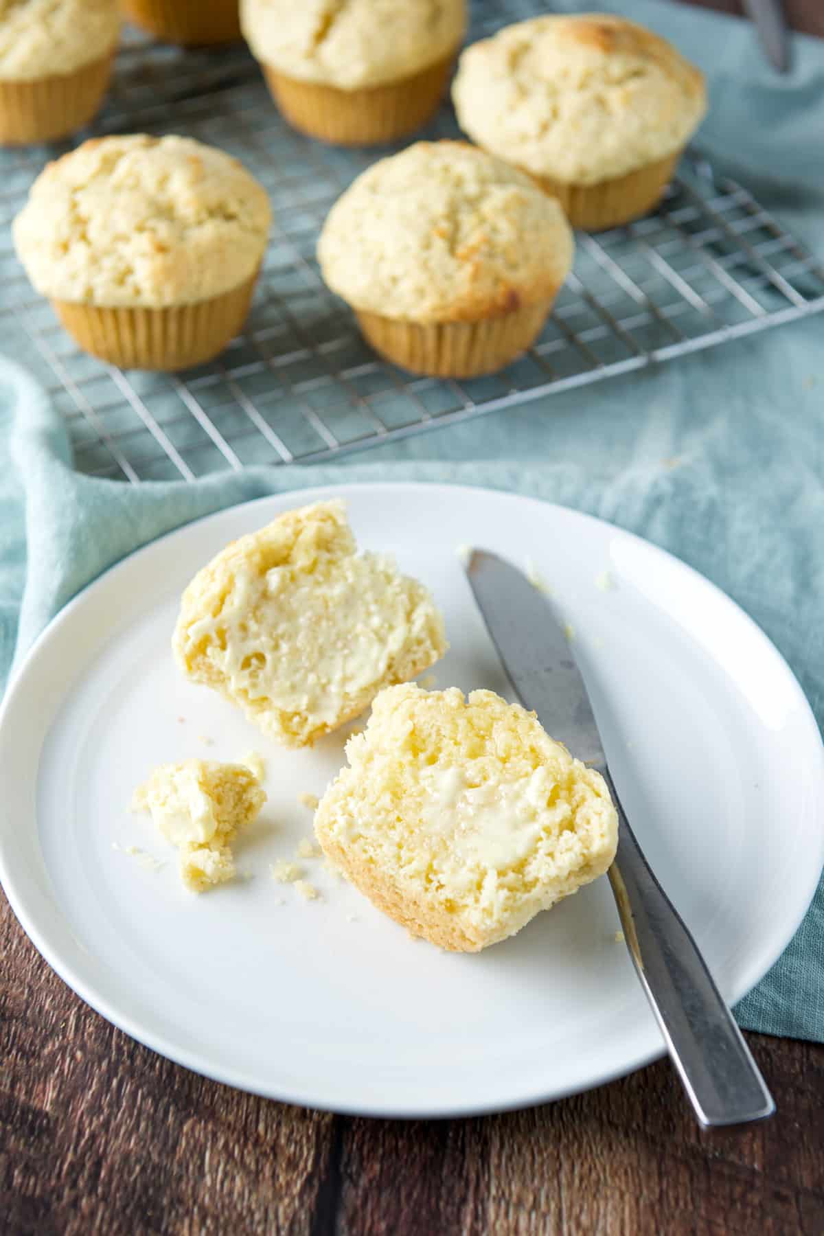 Butter melted on the muffin halves with more muffins behind the plate on a wire rack