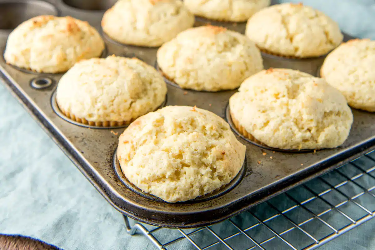 horizontal photo of lemon muffins in a pan cooling on a rack