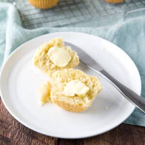 a square photo of a white plate on a green napkin with two halves of a muffin cut in half with butter on them