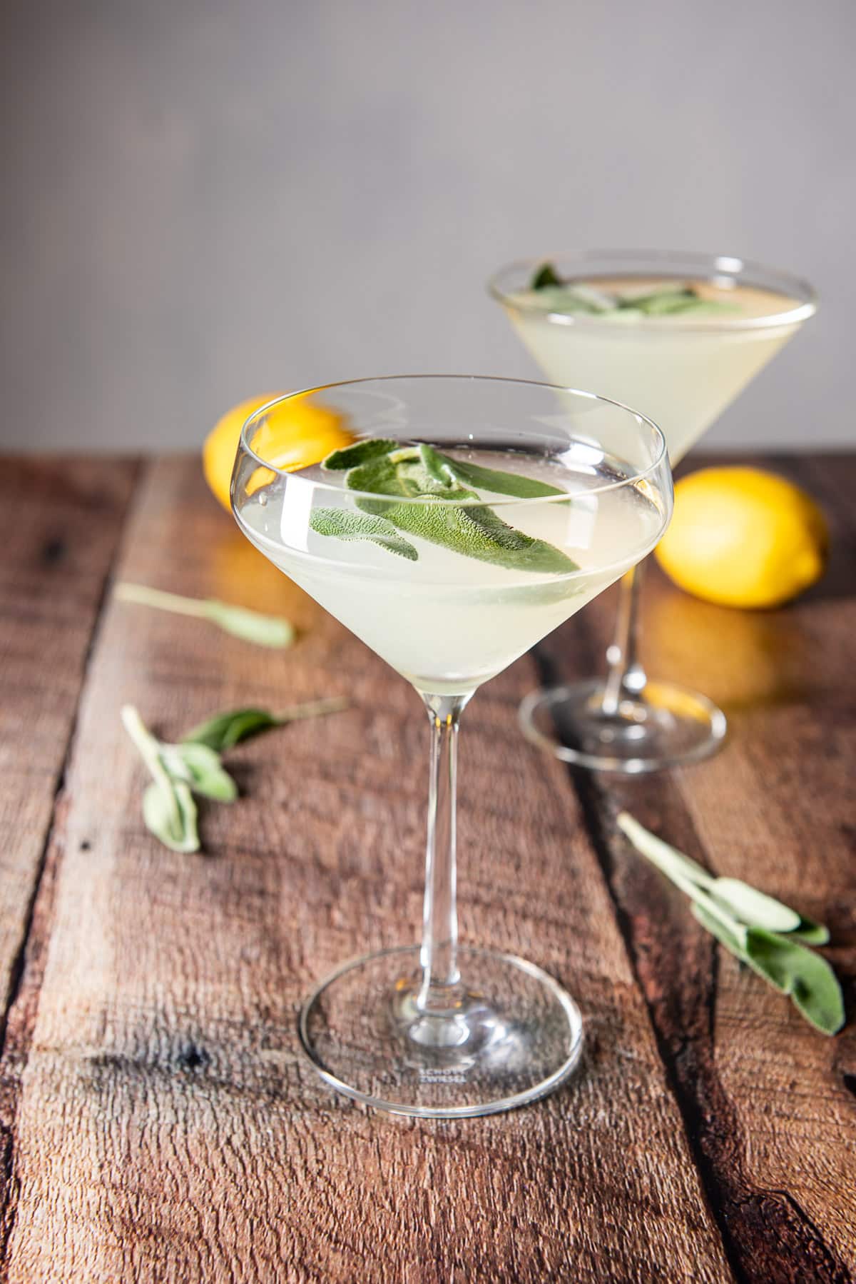 wooden boards with the martini glasses filled with the cocktail along with lemons and sage leaves