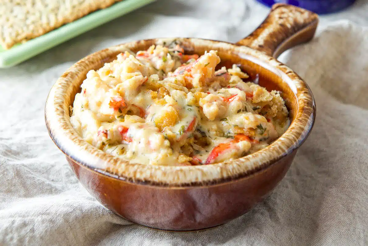 A brown bowl filled with lobster dish and some crackers in back