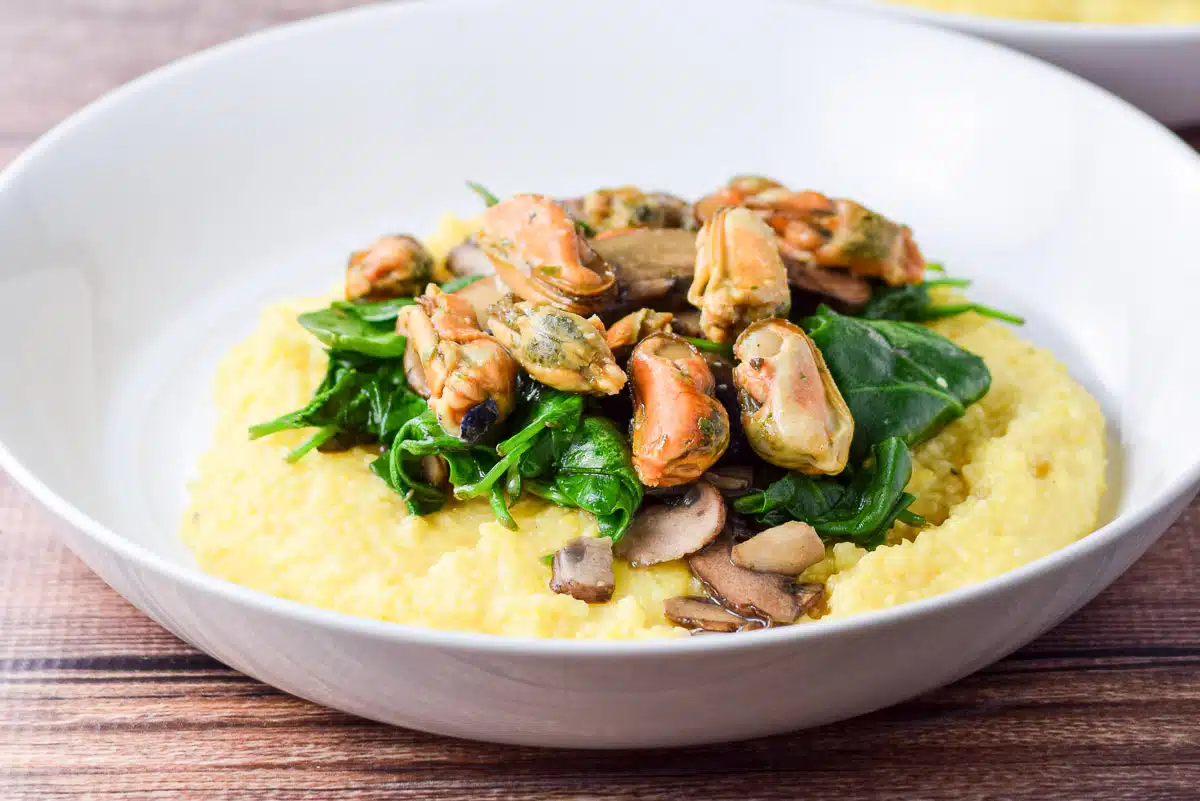 mussels and spinach on polenta in a white bowl