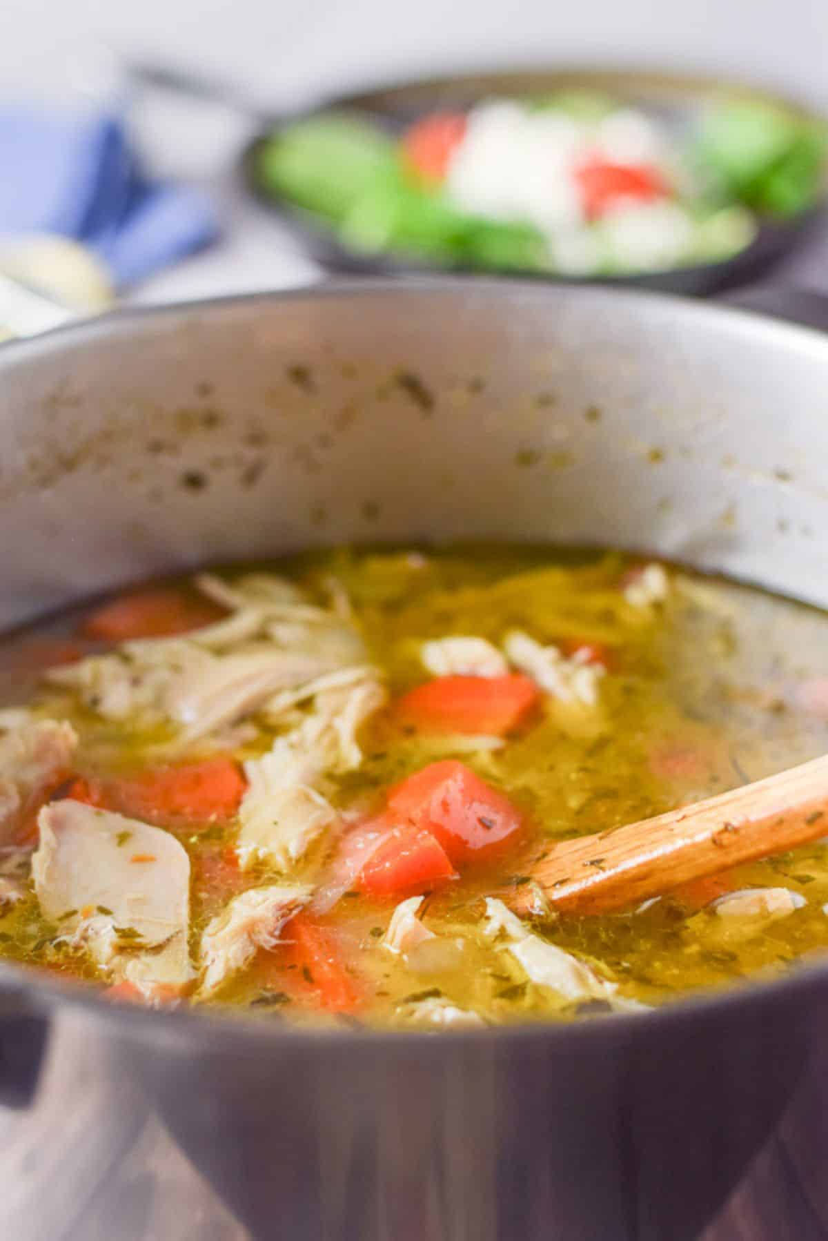 Close up of the chicken soup in the pan with a wooden spoon in it and a salad in the background