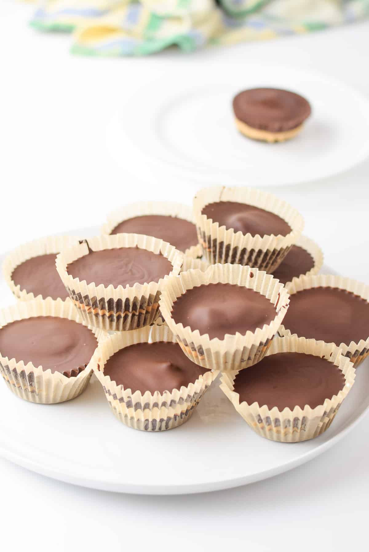 A pile peanut butter cups on a white plate with one in the back