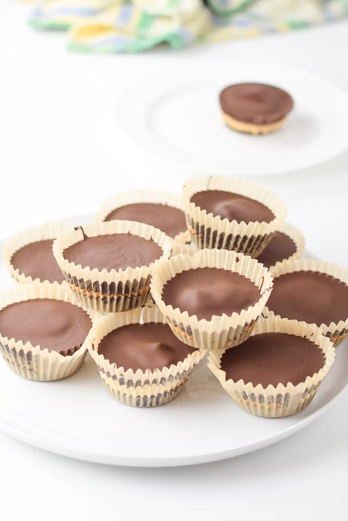 A pile peanut butter cups on a white plate with one in the back