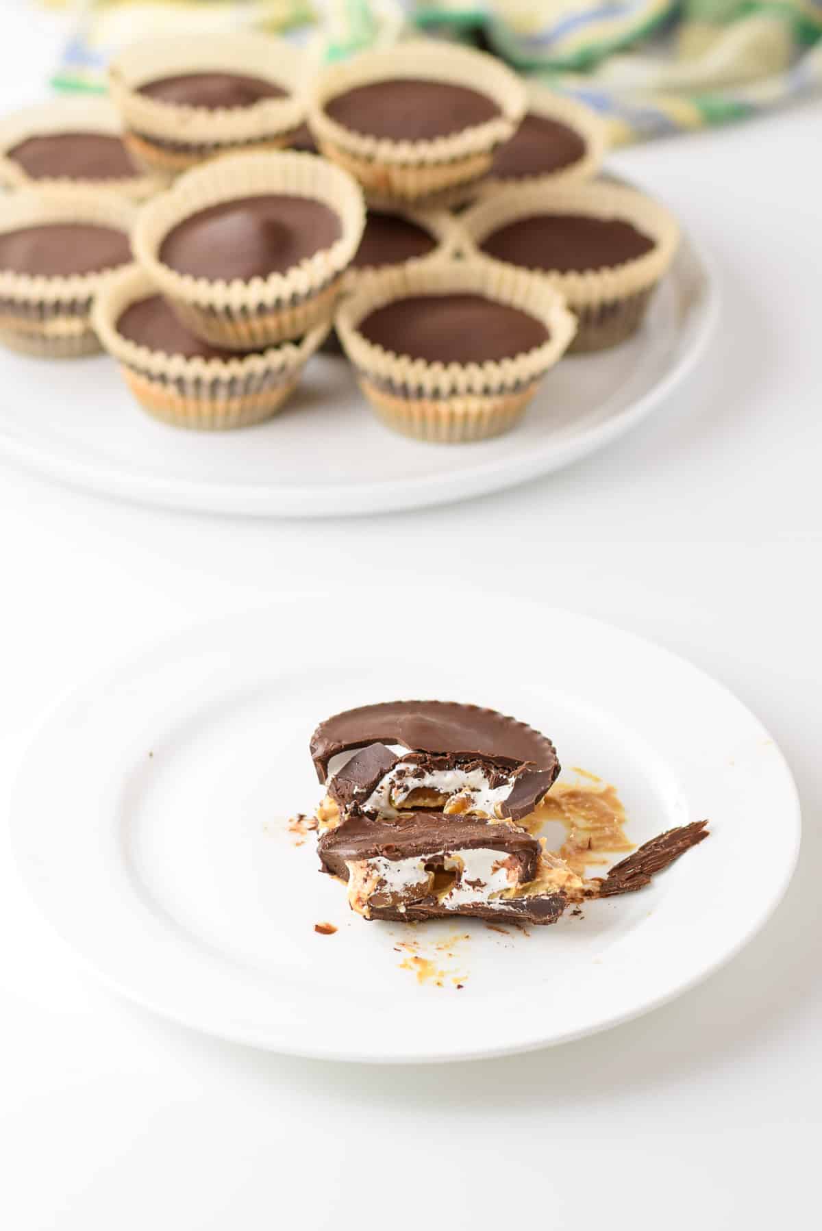 A cracked open marshmallow cup on a white plate with a pile of the cups in the background