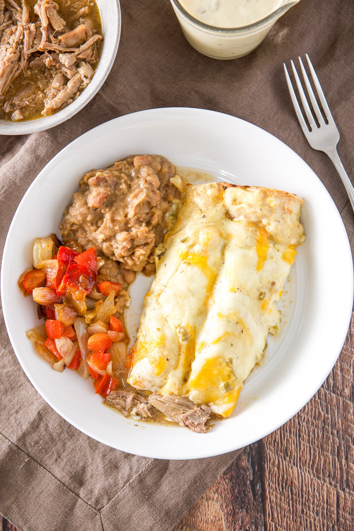 Overhead view of the two enchiladas with beans and veggies on it. There is some pulled pork in the corner
