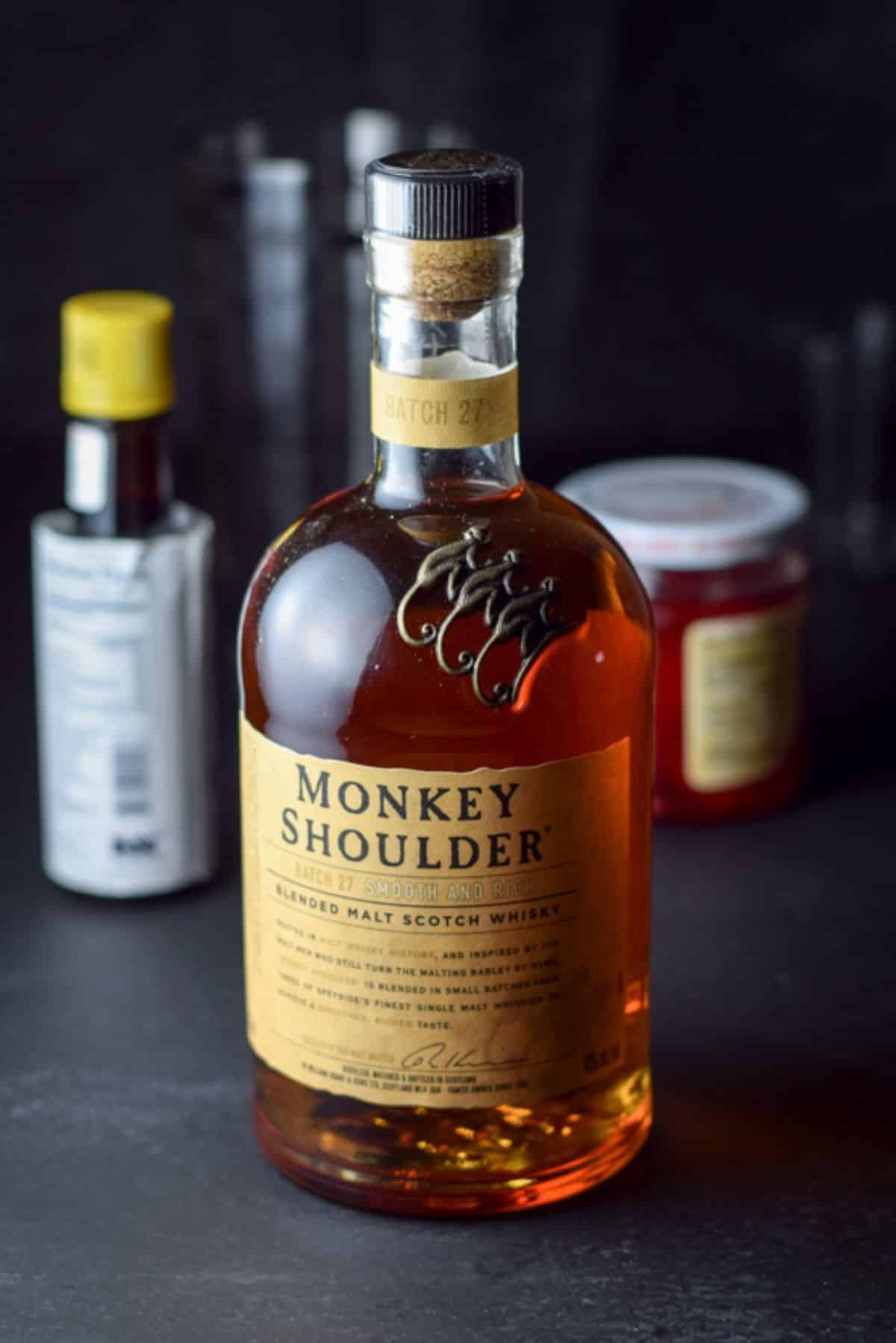 Scotch, bitters and maraschino cherries in the background