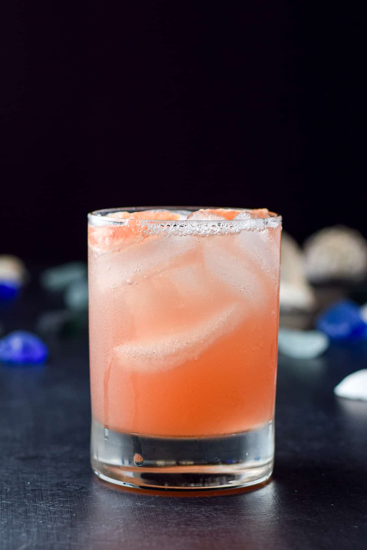 vertical view of the sea breeze cocktail with sea glass and shells behind it