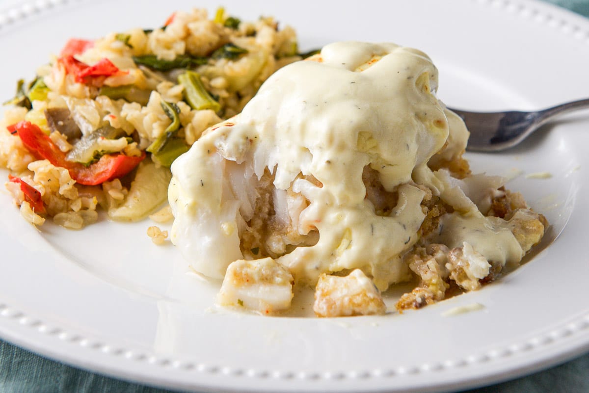 A white beaded plate with sauce covered stuffed fish and rice