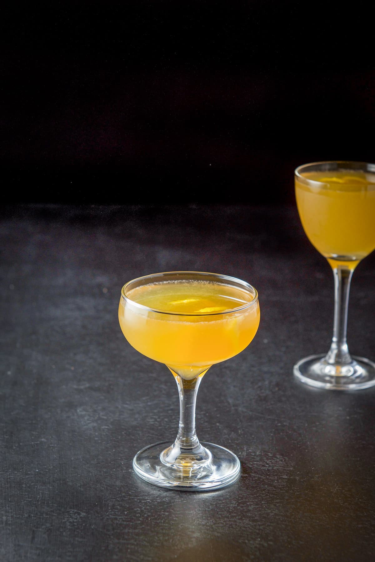 Two coupe glasses filled with the amber cocktail on a black table