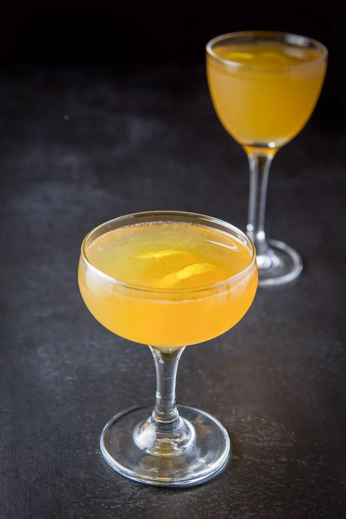 Close view of a coup glass filled with the sidecar cocktail with another glass in back. Both have lemon twists
