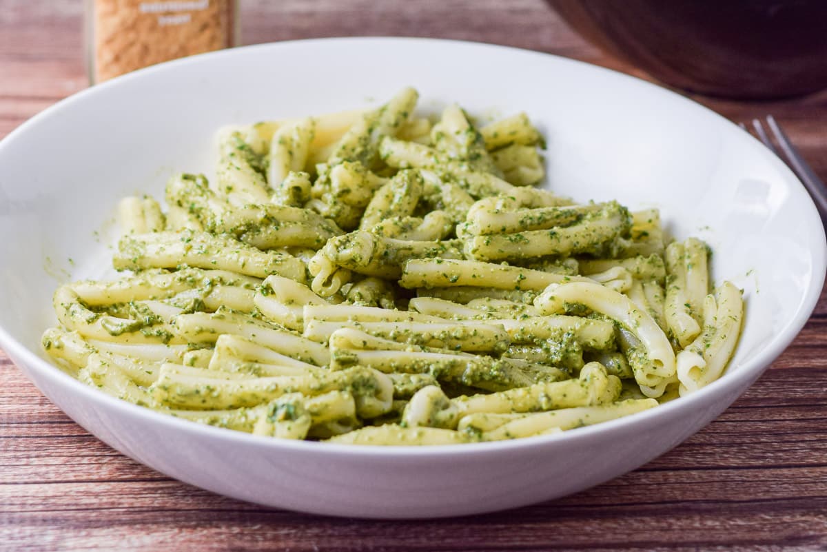 horizontal photo of a white deep dish filled with pasta and pesto