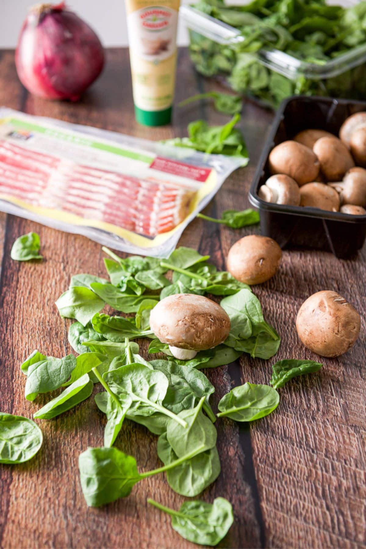 A wood table with spinach, mushrooms, bacon, and red onion