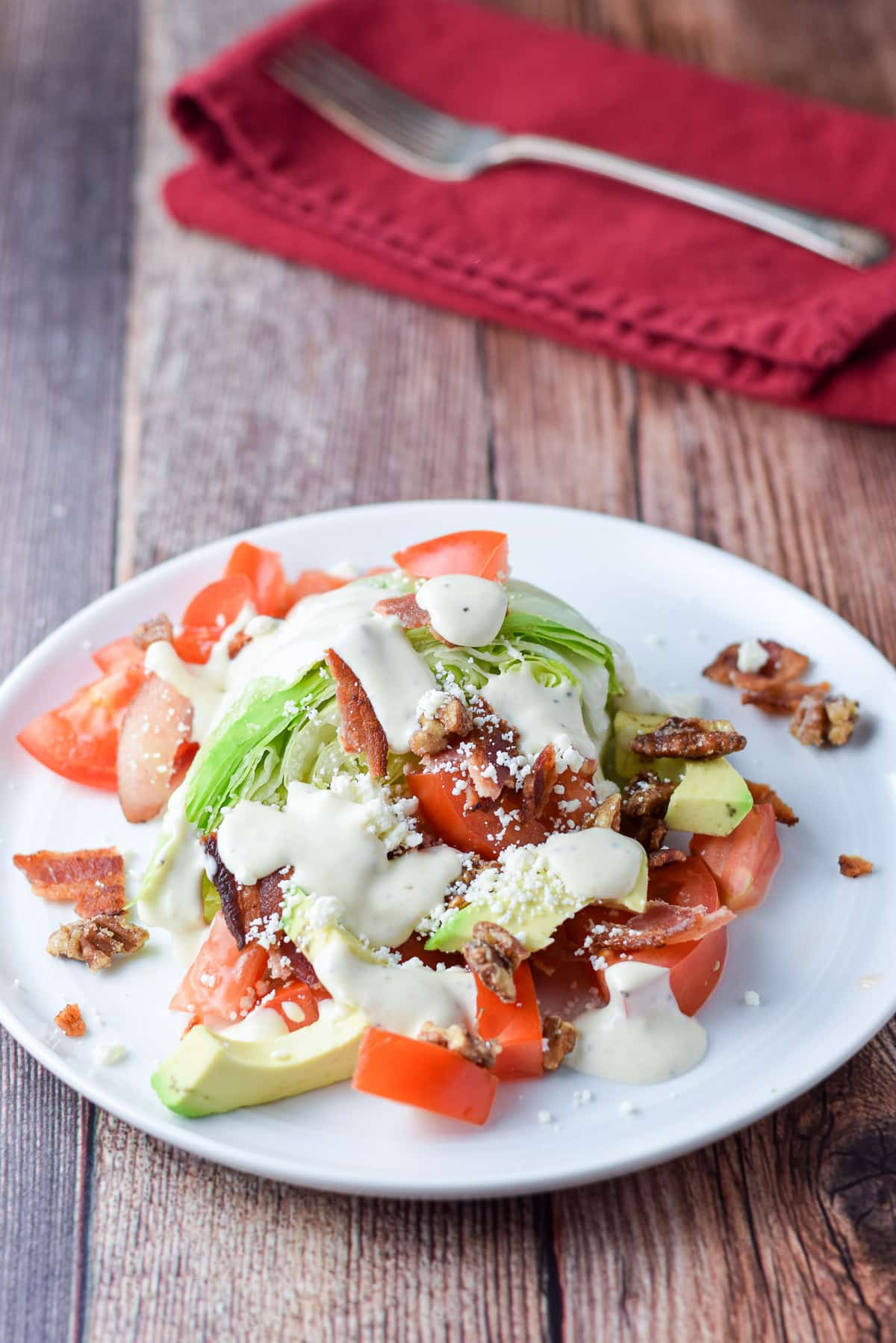 Dressing on the salad that's on a white plate with a napkin and fork in the background