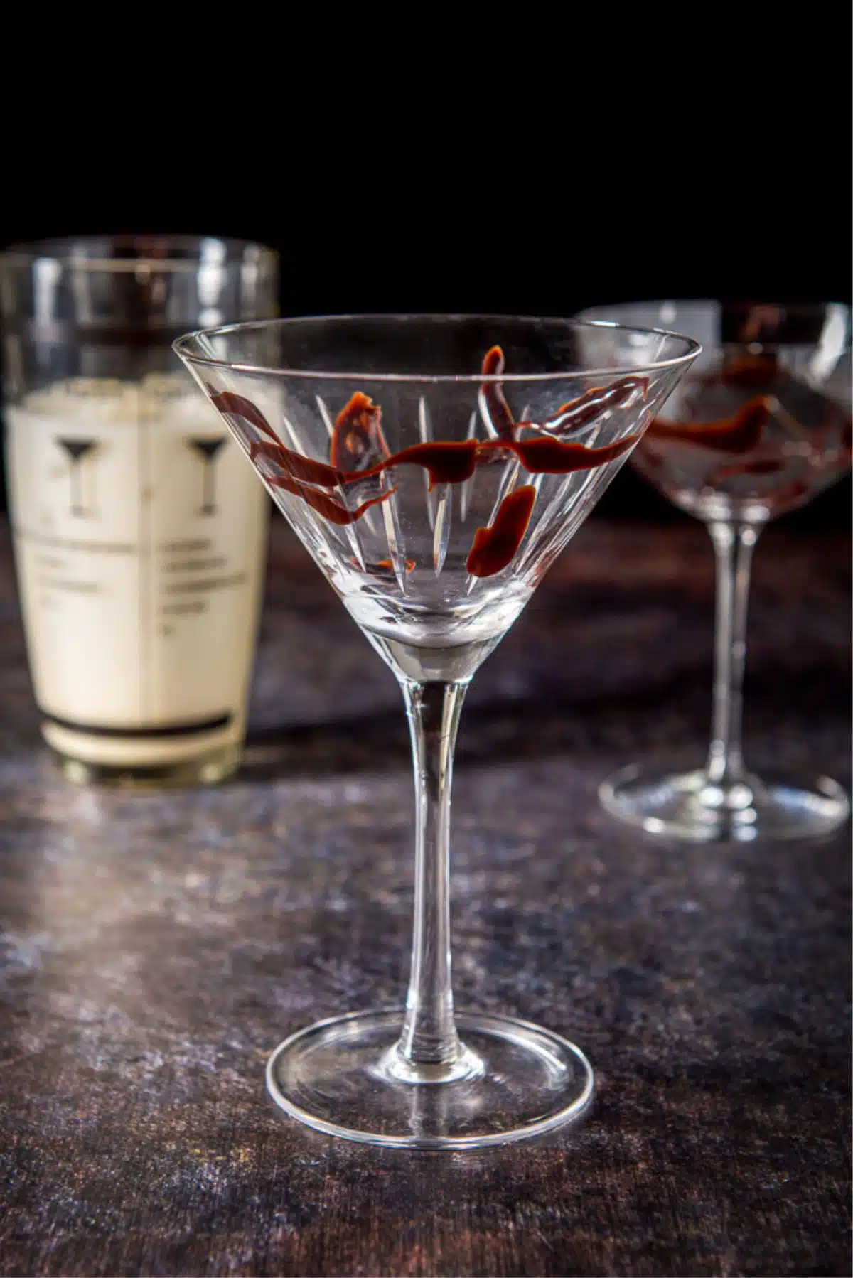Chocolate sauce swirled in the glasses as garnish with the filled shaker in the background